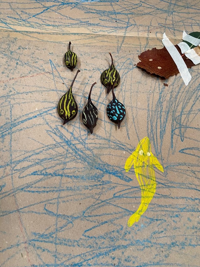 Art Tree photo: Meg Taranto. A child's creation, with seed pods, paint pens, bark, masking tape and pastels on brown cardboard, of corroboree frogs in a stream.