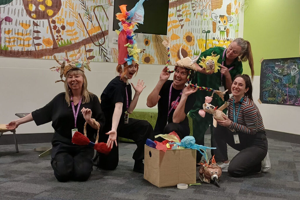 Polyglot Theatre and Centre for Community Child Health personnel pose for the camera, wearing or holding handmade paper creations.