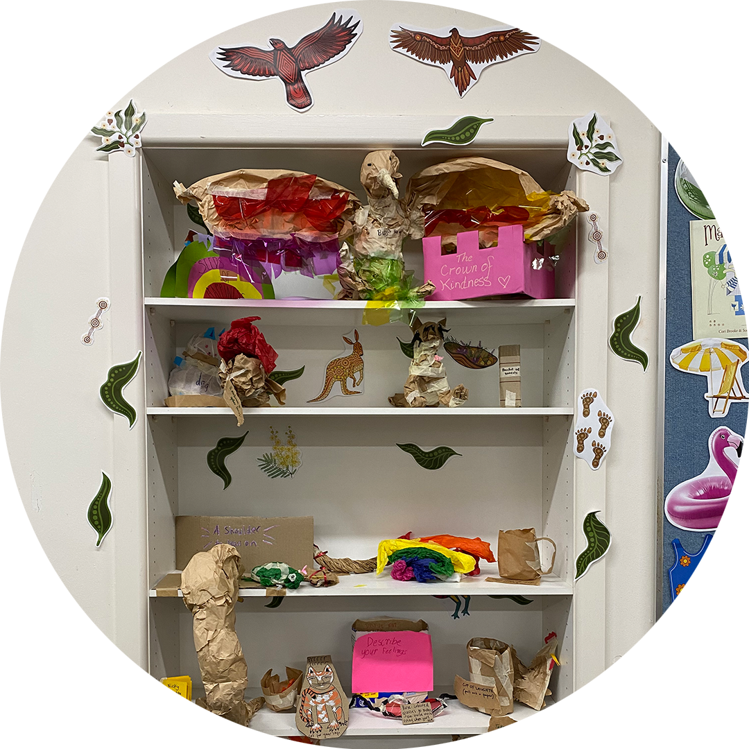 Wish Street production photo: Maisy Butchart. A white bookshelf in the classroom is adorned with paper creations, and surrounded by paper cut outs of birds and leaves.