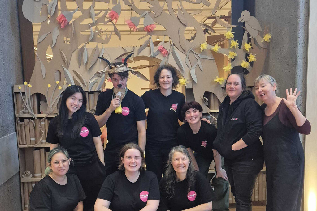 Behind-the-scenes photo. The Polyglot team is gathered in front of the Paper Planet entrance at Wyndham Art Gallery, smiling at the camera.